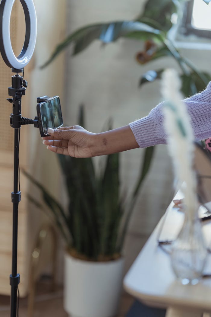 A woman adjusting a smartphone on a ring light stand for video recording indoors, showcasing modern digital creativity.